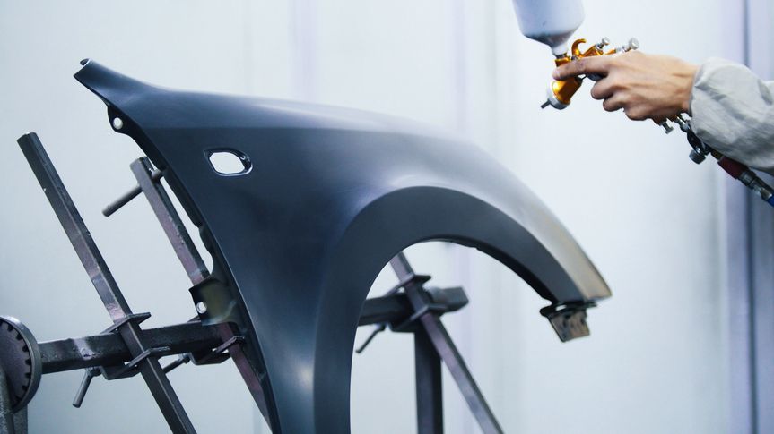 Autolackierer sprüht schwarzen Autokotflügel in Werkstatt